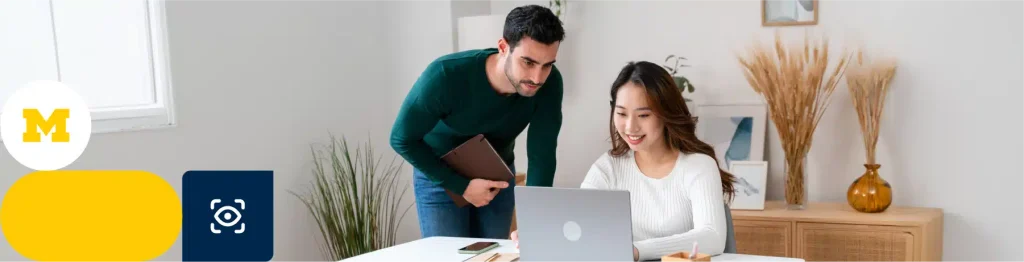 “Two individuals working in an office, one standing with a tablet and the other seated at a laptop.”

